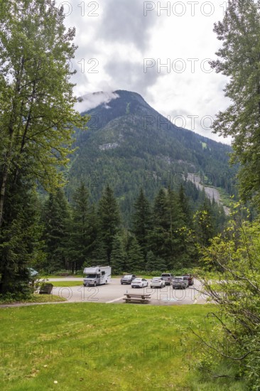 Clouds partially covering mountain peak near parking lot with parked recreational vehicles and cars