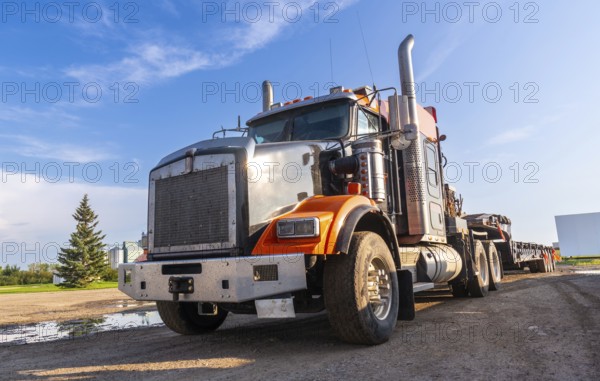Gleaming orange and silver semi truck parked on a gravel road, bathed in the warm glow of late