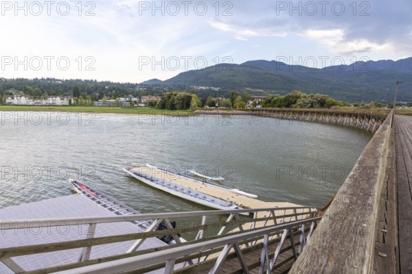Dragon boats are tied up at a floating dock near a wooden pier, with the city of salmon arm and the