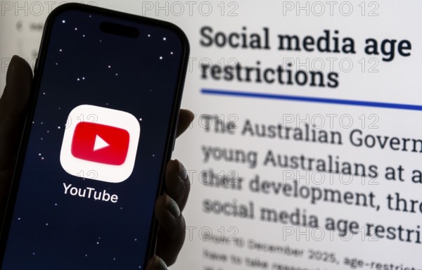 In this photo illustration, a person holds a phone displaying the YouTube app in front of a screen