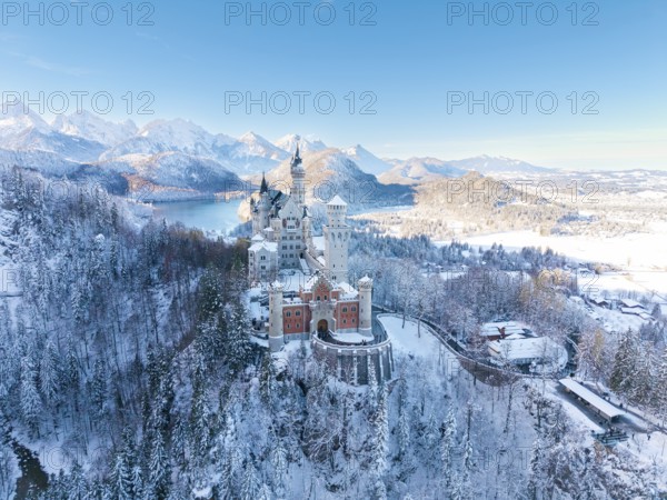 Wintery Neuschwanstein Castle with bright sky, surrounded by snow-capped mountains and forests,