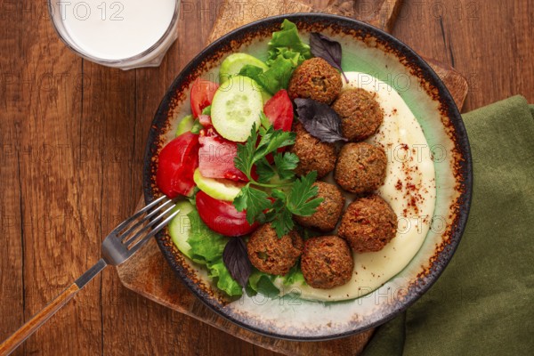 A plate holds falafel balls, tahini, salad with tomatoes and cucumbers, and a drink. The setting is