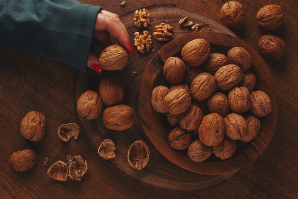 A woman's hand taking a walnut from a wooden bowl filled with walnuts. There are shells and walnuts