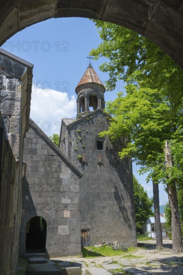 View through an arch of a church with bell tower, surrounded by trees, in shade, Sanahin monastery,