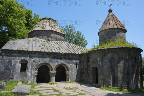 Historic monastery with two domes, overgrown roofs and stone structures under clear skies, Sanahin