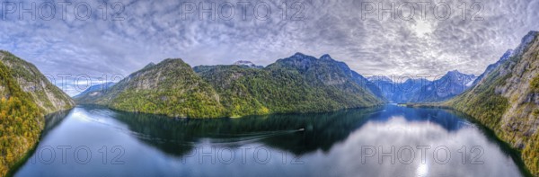 Calm lake with boat surrounded by high mountains and dramatic sky, Germany, Königssee, drone,