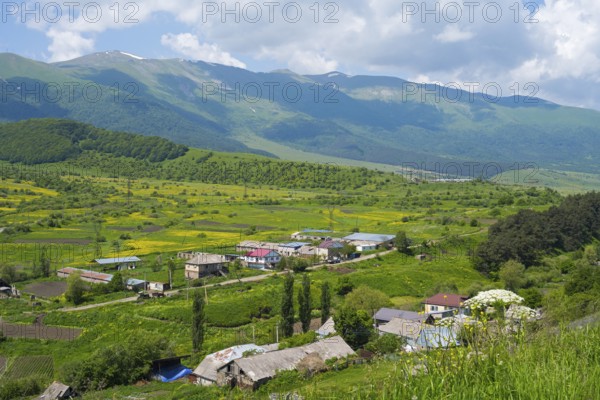 A quiet village in a green valley with mountains and blue sky in the background, Fioletowo,