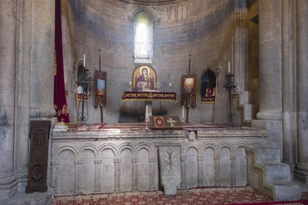 Historic church altar with icons and candles in a stone room, illuminated by windows, Goshavank