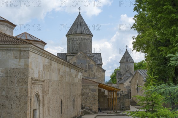 Monastery with stone buildings and towers under partly cloudy sky, surrounded by trees, Haghartsin