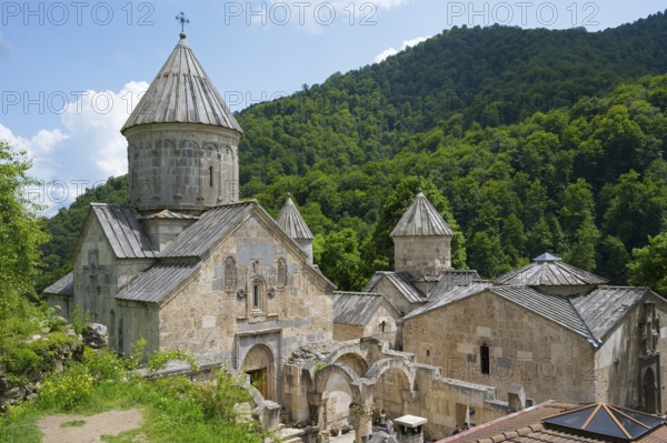Monastery complex on green hill with towers and stone buildings surrounded by forest, Haghartsin
