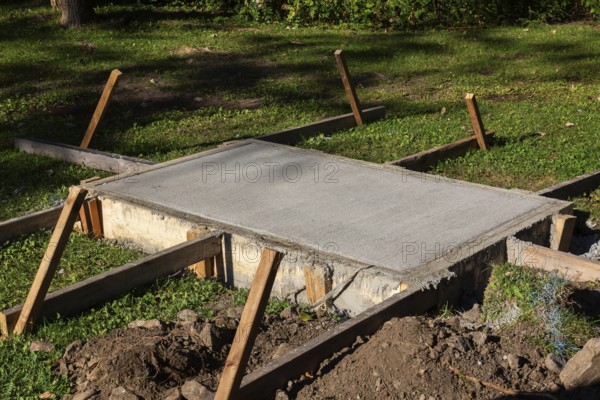 Wooden concrete pouring forms and freshly poured raised concrete base for anchoring a bench in