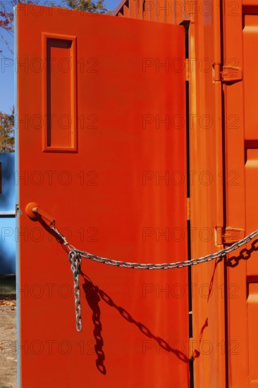 Entrance door kept opened with a chain on bright fluorescent orange painted metal box shaped