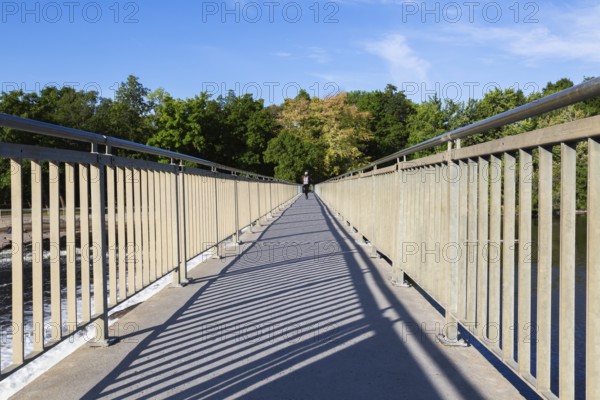 Electric scooter rider on pedestrian walkway on top of water flow control Moulin Neuf dam over Des