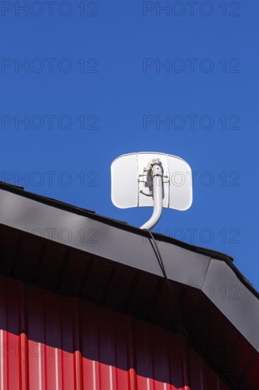White satellite T.V dish antenna installed on gable roof of building cladded with red sheet metal