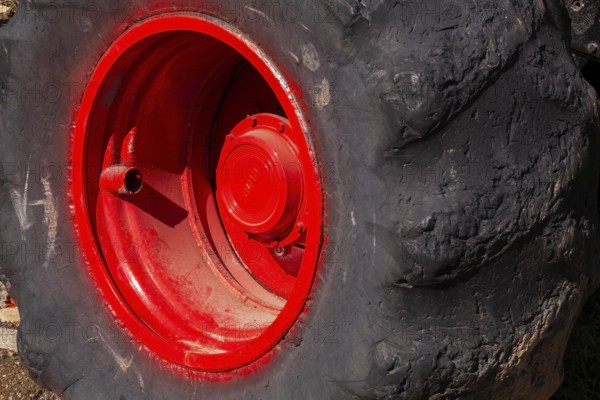 Close-up and rear side view of large heavy duty black rubber tire mounted on red rim on monster
