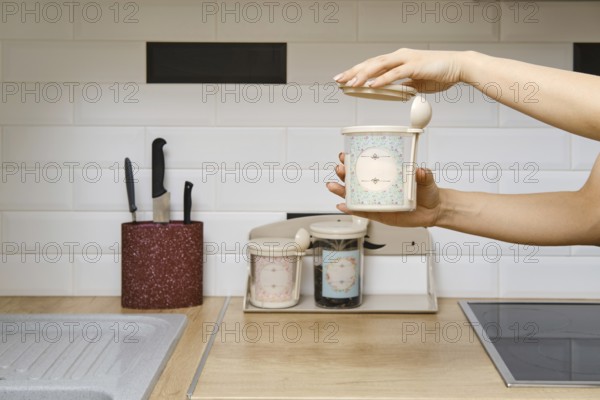 A person holds a container in one hand while opening the lid with the other. The kitchen has a
