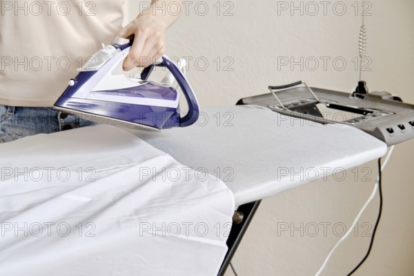A person stands by an ironing board and uses an iron to press a shirt. The setting is a home