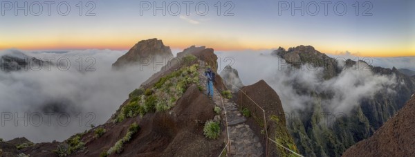 Photographer photographs sunrise at Pico do Arieiro, clouds of fog sweeping over mountain peaks,