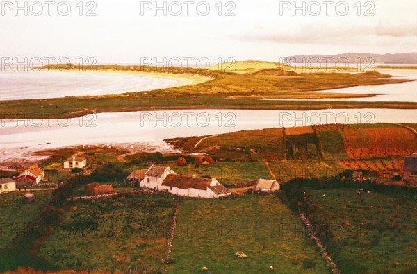 View over thatched farmhouse buildings to Magheraroarty Beach, Meenlaragh, County Donegal, Ireland