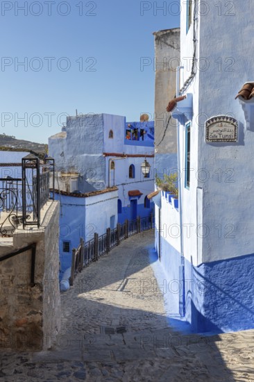 Narrow, winding street in a city with characteristic blue and white buildings under clear skies,