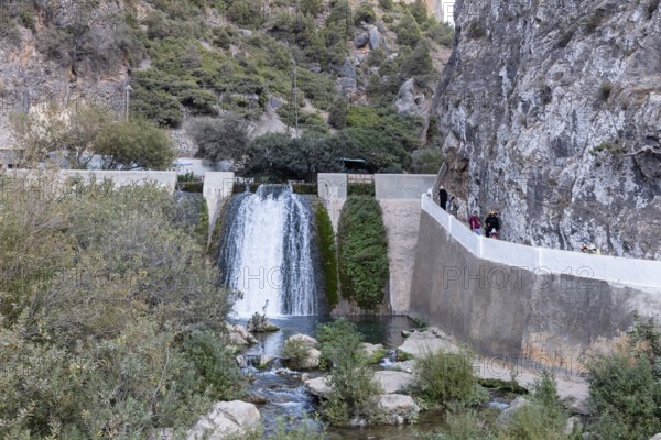 Small waterfall flows through rocky gorge surrounded by vegetation and bounding walls, El Kelaa in