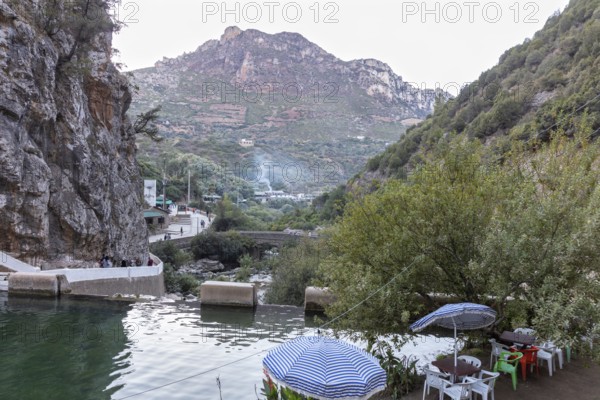 View of a quiet river and road in front of a picturesque mountain panorama with umbrellas, El Kelaa