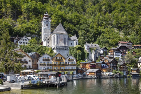 A, Hallstatt, White Church and picturesque houses on the water, surrounded by green mountains,