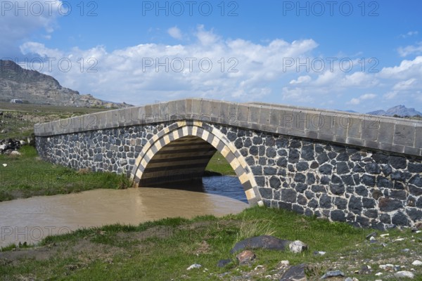 Stone bridge over a river in a green landscape under blue sky, bridge near Cevirme, Dogubayazit,