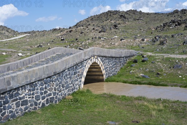 Stone bridge over a small river surrounded by rocky landscape under blue sky, bridge near Cevirme,