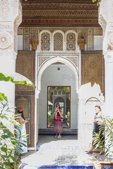 A traditional courtyard with arches, mirrors and decoration and two woman, Bahia Palace in