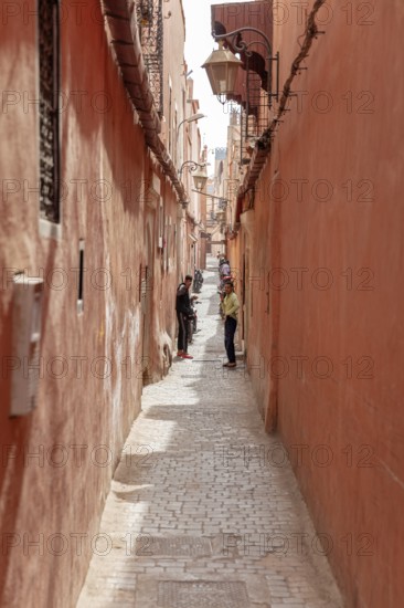 Narrow alley with red walls and walkers on the paved path in an old town