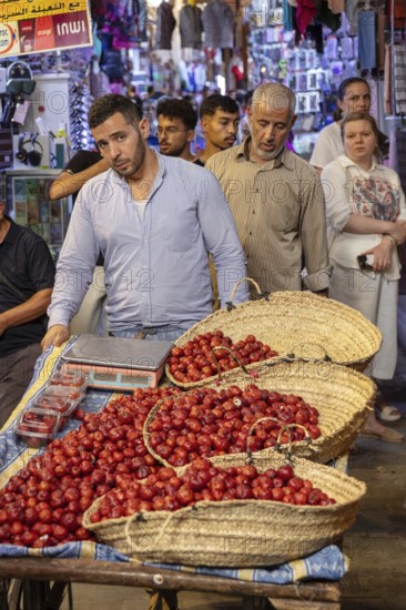 People taste and sell fresh fruit in baskets at a busy market