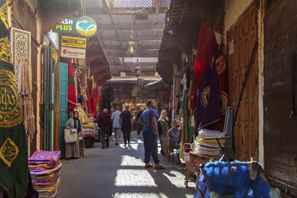 Narrow market street with colorful textiles and carpets, passers-by stroll along