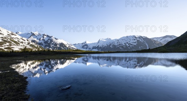 Mountain peaks with Portage Glacier glacier and snow reflected in Divide Lake mountain lake in