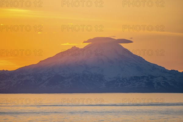 View of Cook Inlet on white mountain peaks of Mount Redoubt at sunset, picturesque golden light of
