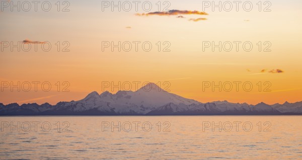 View of Cook Inlet on white mountain peaks of Mount Iliamna at sunset, picturesque golden light of