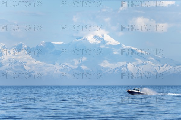 View over Cook Inlet to white mountain peaks of Mount Iliamna, motor boat rides on the ocean,