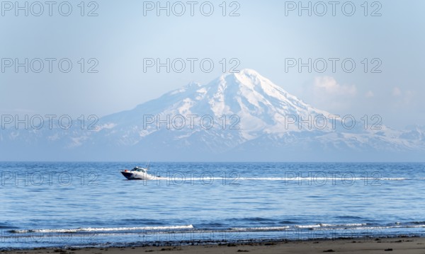 View over Cook Inlet to white mountain peaks of Mount Redoubt, motor boat rides on the ocean,