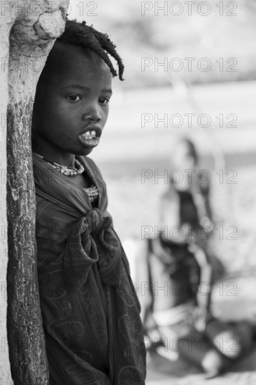 Black and white, Himba girl leaning at a traditional clay hut, in the morning, traditional Himba