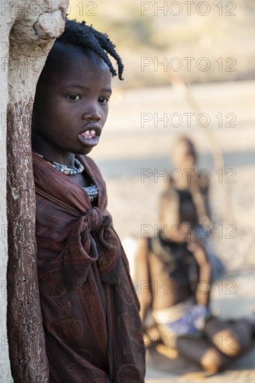 Himba girl leaning at a traditional clay hut, in the morning, traditional Himba village, Kaokoveld,