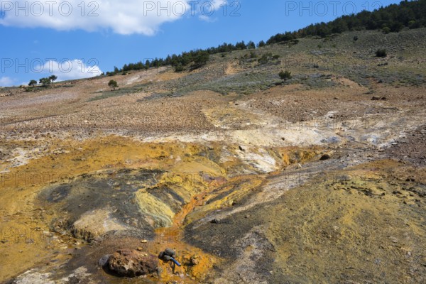 Extensive geological landscape with hills, orange and green areas under blue sky, geothermal area,