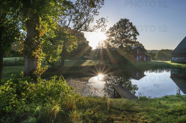 Manor with historic stables and pond, from 1923, in backlight with sun star, Gut Othenstorf,
