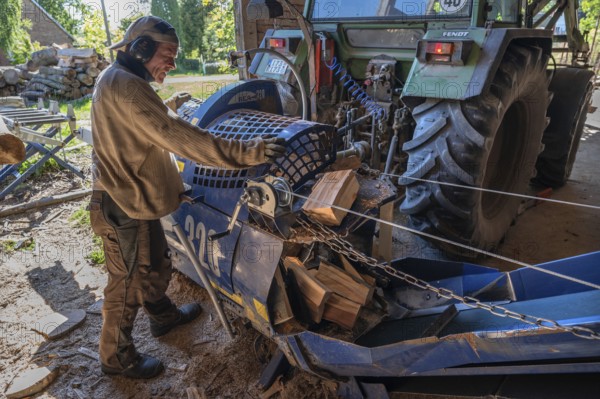 Young man sawing and splitting beech logs with his saw cutting machine, powered by a tractor in a