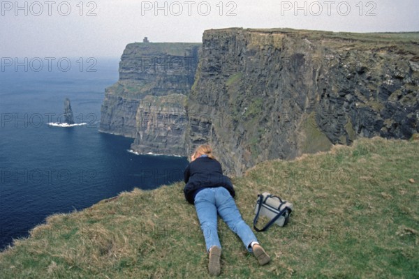 Young woman taking pictures at the edge of a cliff, there was no fence back then, Cliffs of Moher,