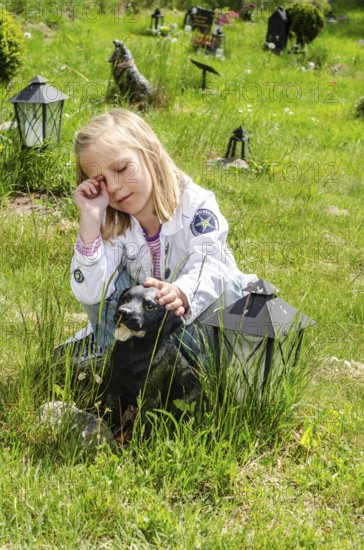 Grieving blonde 7-year-old girl at her dog's grave at pet cemetery in Ystad, Skåne County, Sweden,