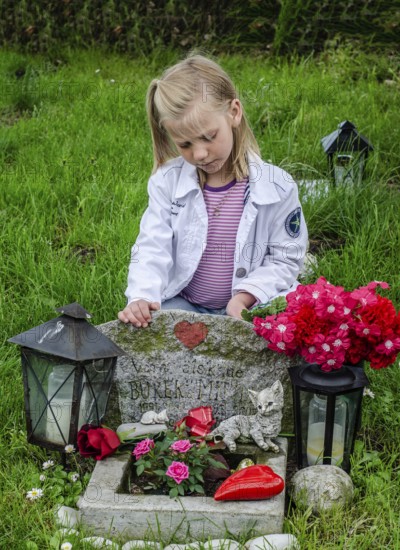 Grieving blonde 7-year-old girl at her cat's grave at pet cemetery in Ystad, Skåne County, Sweden,
