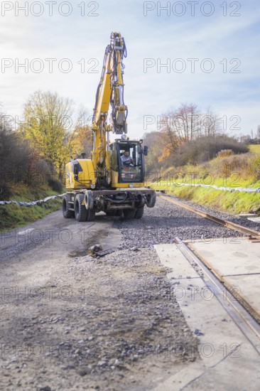 Yellow excavator lays tracks in autumn landscape, preparation of track work, track construction of