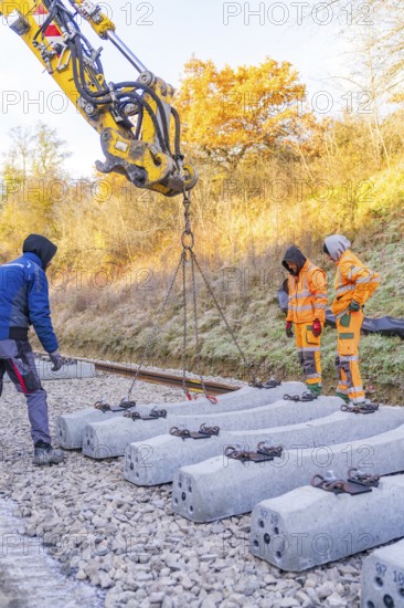 Construction workers supervise the use of an excavator for laying concrete ties, Hermann Hesse