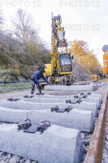 Workers use an excavator to lay concrete blocks along the tracks in autumn surroundings, track