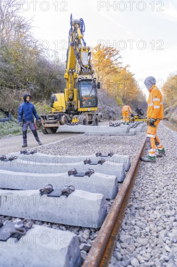 Construction workers lay concrete ties with a yellow excavator on a railway line in autumn, track